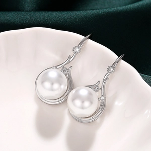 Elegant silver pearl earrings with zircon accents placed on a white ceramic plate