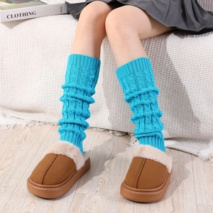 Close-up of blue cable knit leg warmers worn with fuzzy slippers on a wooden floor