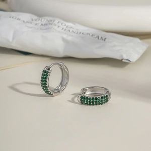 Detail of silver C-shaped earrings set with triple rows of green cubic zirconia stones