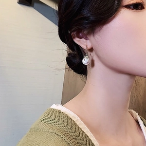 Detailed view of elegant gold C-shaped earring with leaf accent and pearl on a model