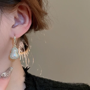 Close-up of elegant gold-rimmed diamond pearl gourd earrings worn by a model