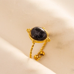 Close-up of gold adjustable ring with oval black marble stone on soft beige fabric