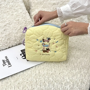 Close-up of cream quilted cosmetic bag with dachshund embroidery and purple zipper pull