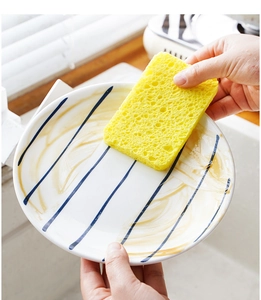 Close-up of a hand using a yellow wood pulp sponge to clean a ceramic dish in the kitchen