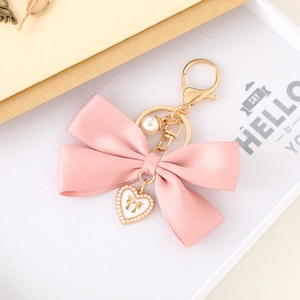 Detailed macro view of pink satin ribbon bow keychain with white enamel heart and pearl