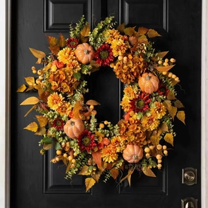 Autumn harvest wreath with pumpkins berries and maple leaves hanging on a black door