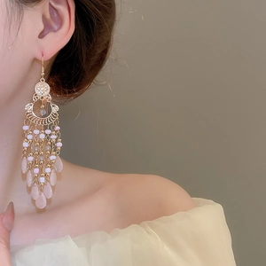 Detail of bohemian drop earrings featuring pink and white beads with gold tassels