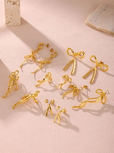 Detailed view of 18K gold plated bow earrings with white rhinestones on pink texture