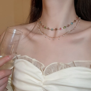 Detail einer zweilagigen Goldkette mit bunten Edelsteinen und kleinen weißen Perlen am Model
