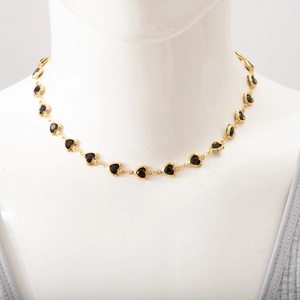 Detail shot of a gold heart-shaped necklace with black gems on a white mannequin