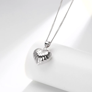 Macro shot of silver heart pendant with radial texture on minimalist white stand