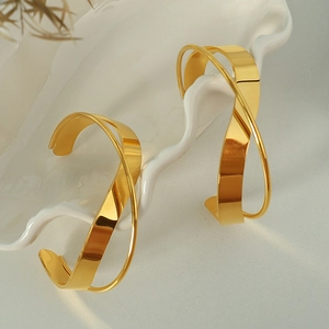 Minimalist intertwined gold open hoop earrings with high-polish mirror finish in ceramic tray