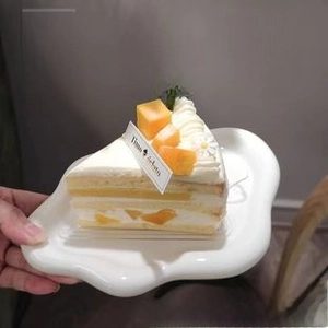 Irregular wave edge ceramic dessert plate held in hand with a piece of mango cake