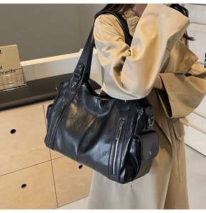 Side view of black faux leather tote bag with silver zippers on beige trench coat
