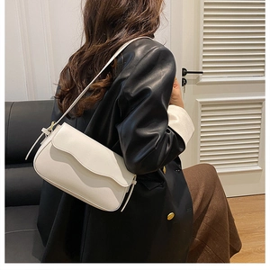 Close-up of a minimalist white leather shoulder bag worn by a model in a home setting
