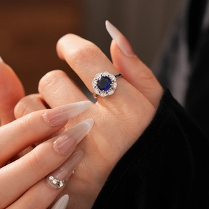Detailed view of vintage hollow diamond flower ring with sapphire blue zircon on finger