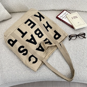 Close-up of khaki canvas tote bag featuring black letter print on cozy white surface