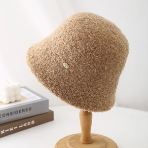 Close-up of camel sherpa bucket hat with a gold metal logo tag on a wooden stand