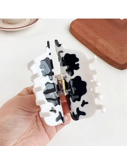 Close-up of handmade cow print acetate hair claw clip held over a wooden heart tray