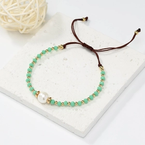 Detail of mint green beaded bracelet with white pearl and adjustable cord on stone surface