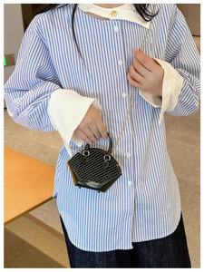 Detail of a black mini shell bag with gold chain strap held by a model in a striped shirt