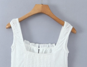 Close-up of white cotton dress featuring delicate lace trim neckline and pleated bust detail