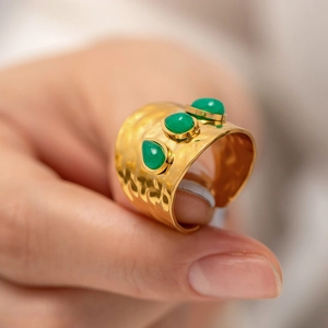 Détail d'une bague dorée texturée au marteau avec trois pierres précieuses vertes
