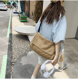 Close-up of beige canvas crossbody bag with black strap in a stylish street style setting