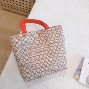 Detailed macro view of small floral canvas tote with red handles and metal snap closure
