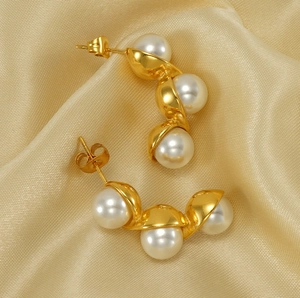 Detail of gold-plated pea pod pearl earrings resting on luxurious golden silk fabric