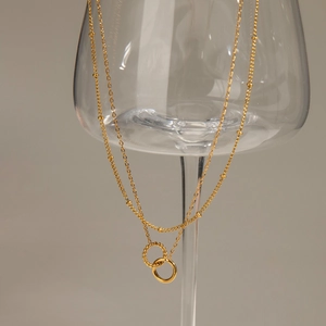 Detailed shot of double-layered gold necklace with interlocking rings on a glass stem
