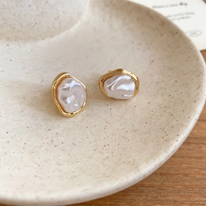 Close-up of French vintage irregular pearl earrings in gold frame on a ceramic plate