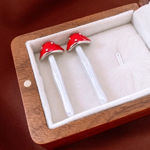 Detailed macro view of red mushroom earrings with white dots in a wooden jewelry box