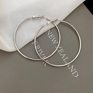 Macro detail of large silver hoop earrings with a polished metallic finish on soft fabric