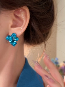 Close-up of blue geometric crystal stud earrings worn by a model in soft natural light
