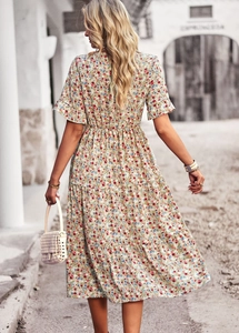 Back view of a flowing beige floral V-neck midi dress on a model walking outdoors