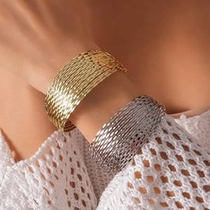 Close-up of layered metallic geometric cuff bracelets in gold and silver finish
