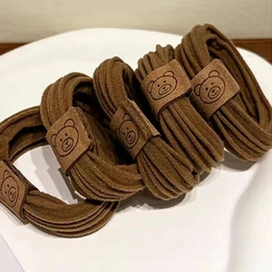 Detailansicht brauner elastischer Haargummis mit geprägtem Bärenkopf aus Leder