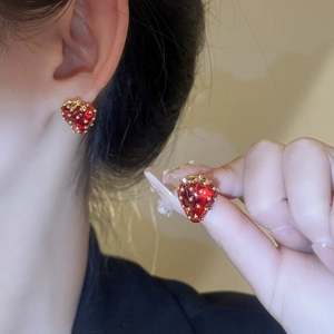 Detailed close-up of cute strawberry stud earrings with red enamel and golden accents