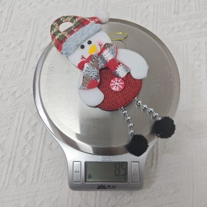 Detailaufnahme eines Stoff-Schneemann-Weihnachtsschmucks auf einer Waage mit 8,5g Gewicht