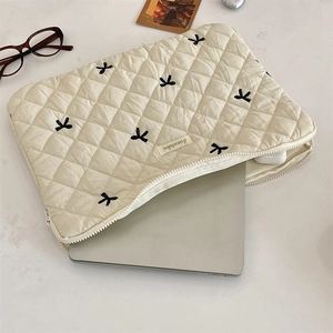 Inside view of beige quilted laptop sleeve with bow embroidery and silver notebook