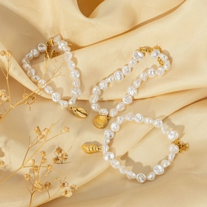 Three-piece baroque pearl bracelet set with gold seashell charms on satin fabric