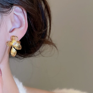Close-up of model wearing gold hollow flower stud earrings with zircon center