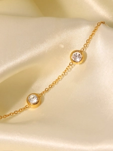 Détail du bracelet en acier doré 18K avec zircons ronds sur un fond en satin beige