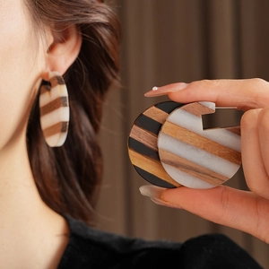 Detail of round geometric earrings with alternating wood and resin stripes on a model