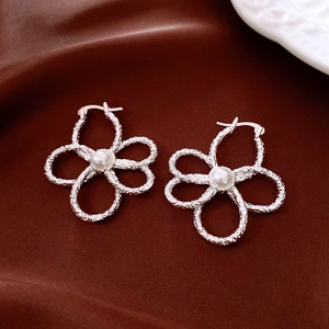 Close-up of silver hollow flower earrings with pearls on dark red velvet background