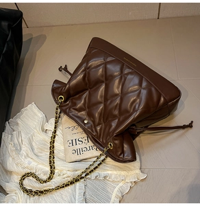 Detail of quilted brown leather bucket bag with chain strap and drawstring closure