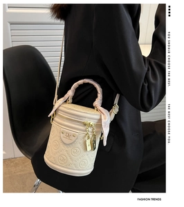 Detail of cream barrel bag with embossed patterns, silk-wrapped handle and gold hardware