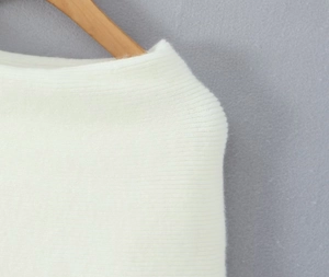 Detailed view of white knitted dress neckline on wooden hanger showing texture