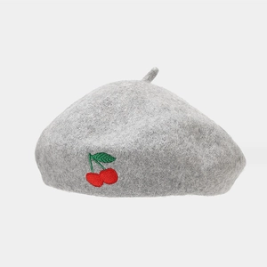 Close-up of a grey wool beret featuring detailed red cherry embroidery and fiber texture
